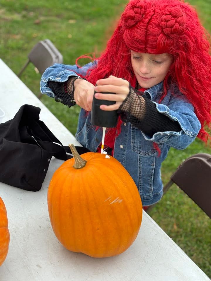 A child in costume decorating a pumpkin